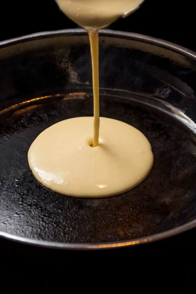 Pancake batter being poured onto a hot griddle pan