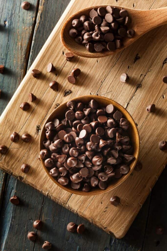 Chocolate chips in a bowl and spoon on top of a cutting board