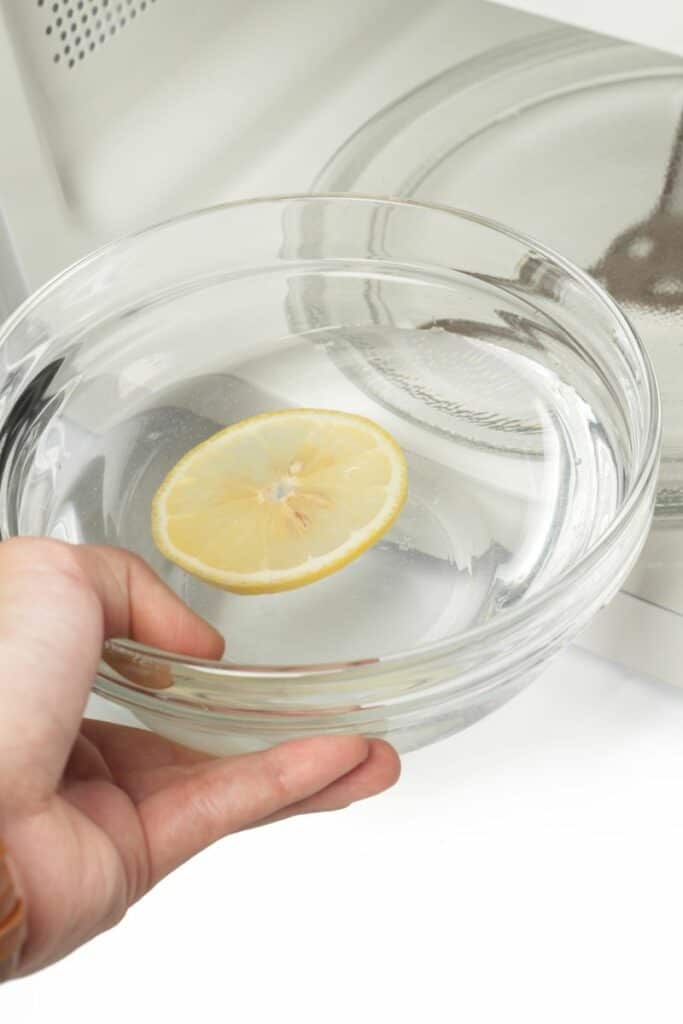 Bowl of water with a slice of lemon being placed in the microwave