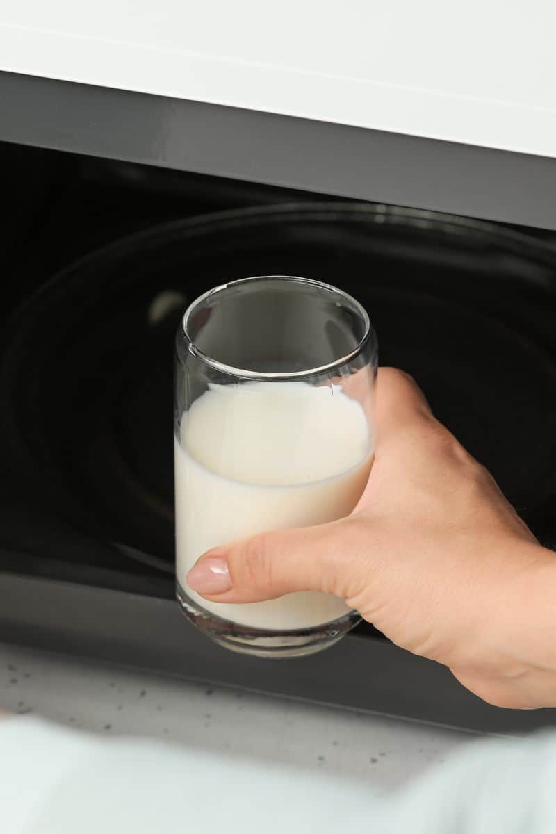 Glass cup with milk being put into the microwave