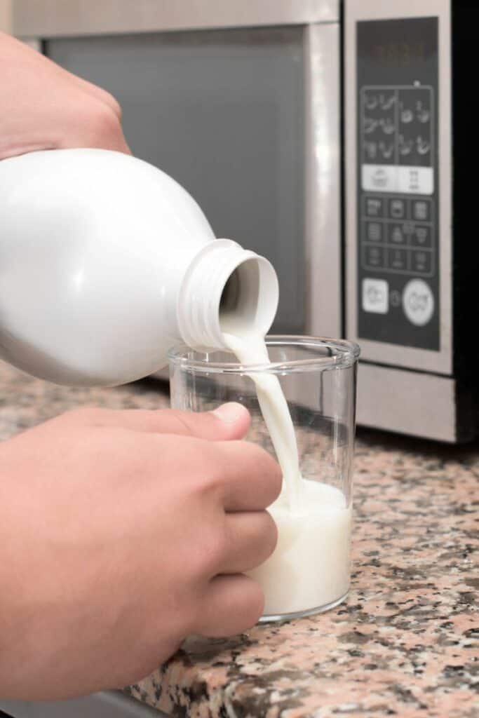 Milk being poured into a glass in front of a microwave